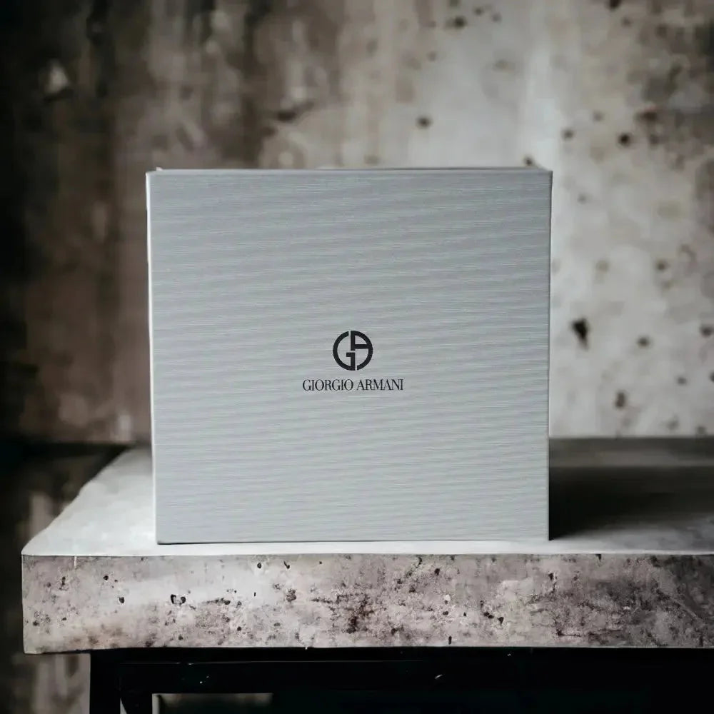 Elegante, hellgraue Geschenkbox mit Giorgio Armani Logo für Parfum Set, auf Steinoberfläche.