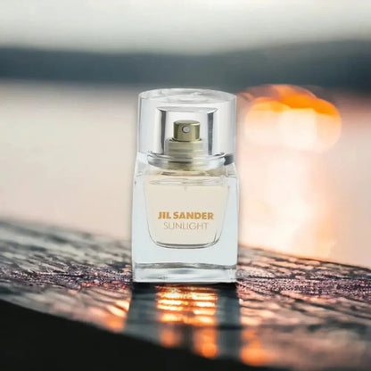 Jil Sander Sunlight Eau de Parfum Flakon auf reflektierender Oberfläche vor Sonnenuntergang