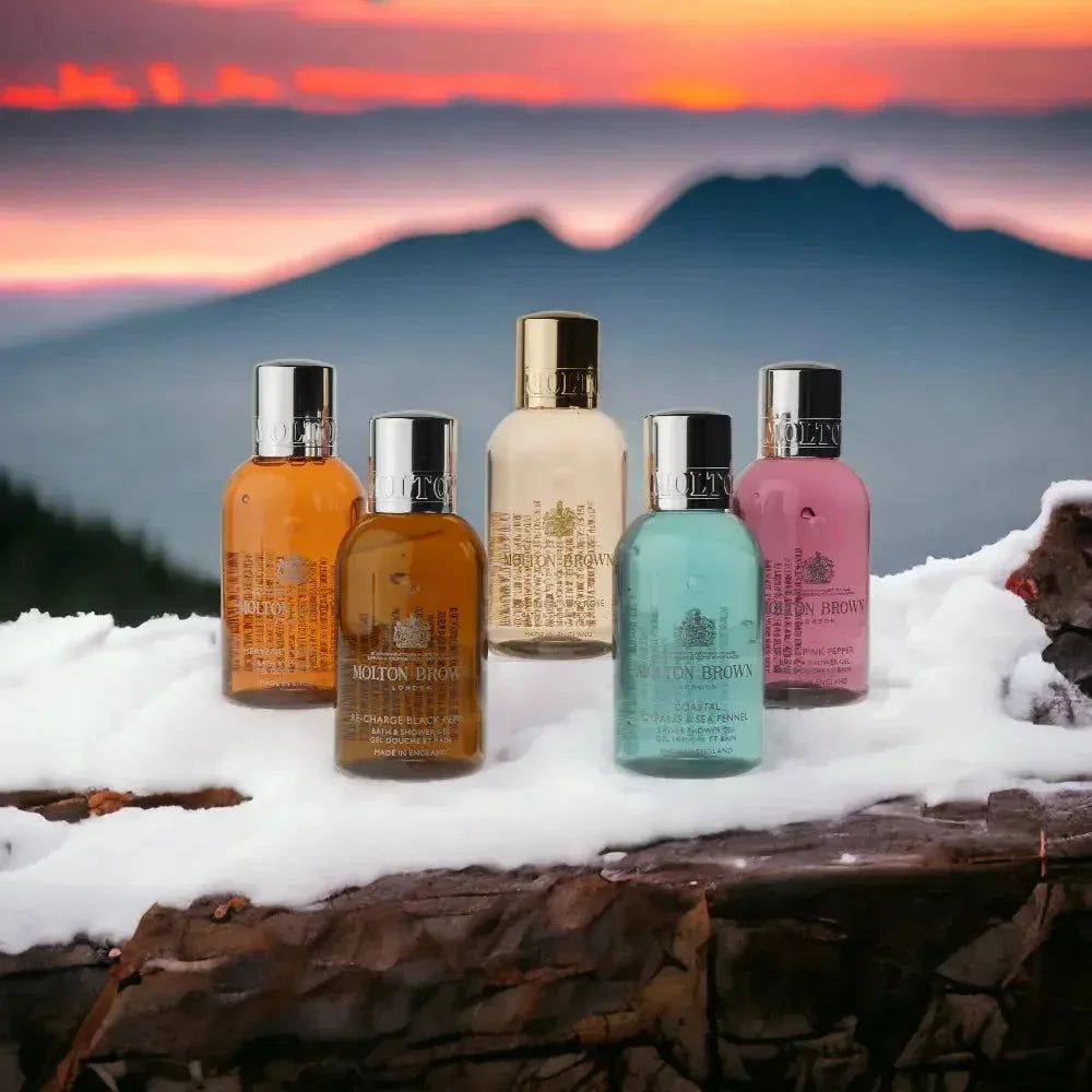 Fünf Molton Brown Duschgel-Flakons in verschiedenen Farben auf Schnee vor Bergpanorama bei Sonnenuntergang.